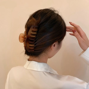 Détail d'une grande pince à cheveux ambre fixant un chignon sur la tête du modèle
