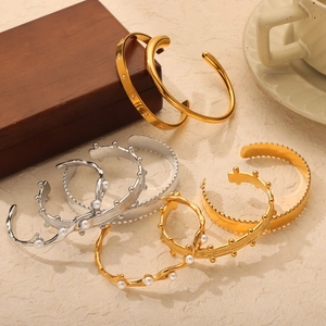 Gold and silver geometric titanium steel cuffs with pearl and rivet details on wood