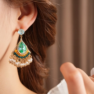 Dettaglio di orecchini vintage dorati con gemme verdi e nappe di perle eleganti su una modella