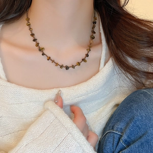 Gros plan d'un collier en œil de tigre sur un mannequin portant un pull blanc