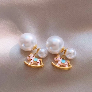 Detailed shot of pink enamel rocking horse earrings with pearls on silk background