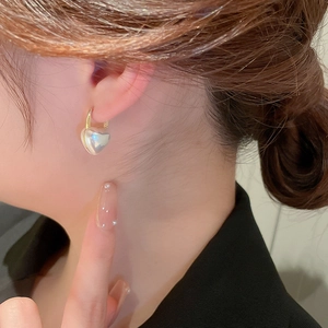 Gros plan d'une boucle d'oreille dorée avec perle en forme de cœur portée par un modèle