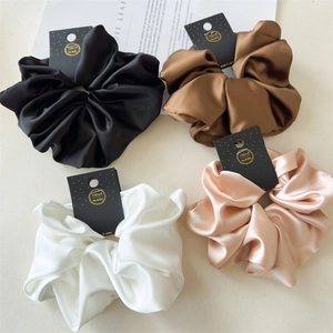 Flat lay of four satin oversized scrunchies in black, brown, white and champagne colors