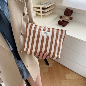 Brown and white striped canvas cosmetic bag held by a model in a blazer for daily use