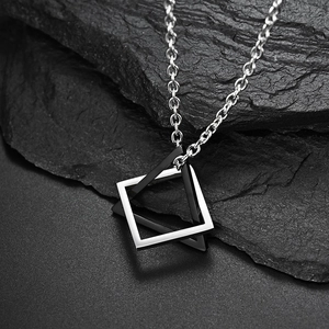 Macro shot of silver interlocking square and triangle pendant on a textured dark rock
