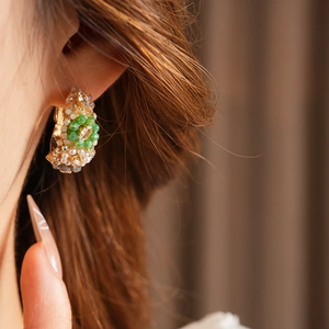 Close-up of vintage beaded hoop earring with green and white faceted crystals on model