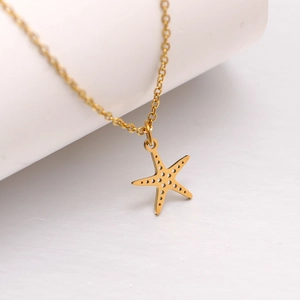 Détail macro du collier pendentif étoile de mer dorée avec découpes sur socle blanc