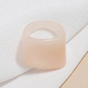 Detail of a light peach pink translucent wide resin ring on soft white fabric background