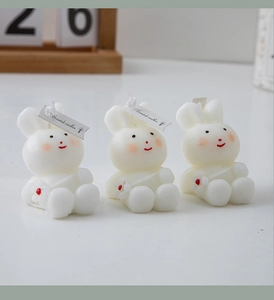 Detailed view of three white rabbit scented candles with pink blush and red flowers