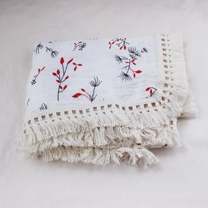 Detail of soft cotton baby blanket with red leaf print and beige handmade tassels