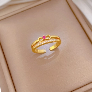 Close-up of golden bow-knot ring with a red gemstone and white cubic zirconia accents