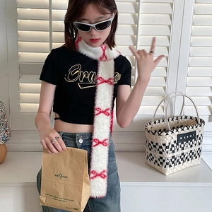 Detail view of a white plush scarf featuring red bow patterns on a street style model