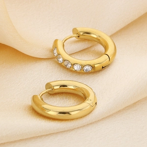 Detail shot of golden U-shaped hoop earrings with clear stones on silk fabric