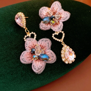 Detailed close-up of pink embroidered flower earrings with teardrop gems on green velvet