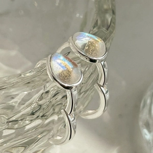 Macro shot of silver teardrop earrings with iridescent moonstone on a glass rim