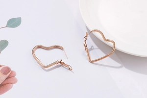Detail of rose gold heart hoop earrings with intricate twisted rope texture pattern