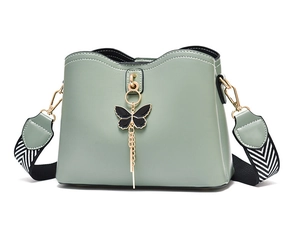 Detail of light green PU leather bag with butterfly pendant and woven shoulder strap