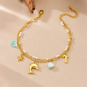 Double-layered gold anklet with shell star and dolphin charms on sandy beach background
