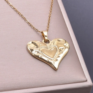 Macro detail of golden double-heart necklace on soft pink jewelry box surface