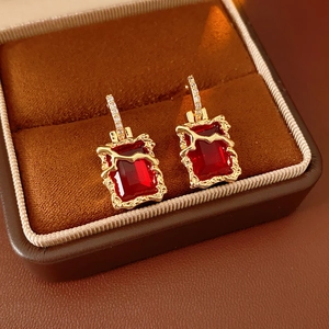 Détail de boucles d'oreilles carrées dorées avec pierres rouges sur velours marron