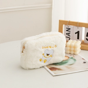 Close-up of white plush cosmetic bag with bear embroidery and elegant pearl zipper pull