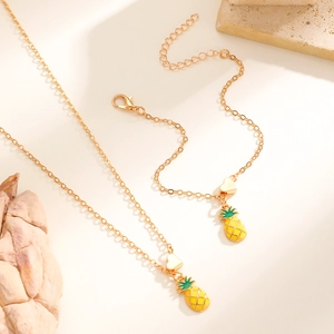Dettaglio di ciondoli a forma di ananas e cuore su un set di collana e bracciale alla moda