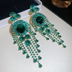 Macro detail of emerald green rhinestone tassel earrings with golden geometric finish