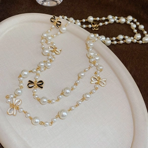 Detail of elegant pearl necklace with black and white bow pendants on a beige tray