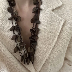 Collana boho multistrato con pendenti in guscio di cocco su giacca di tweed