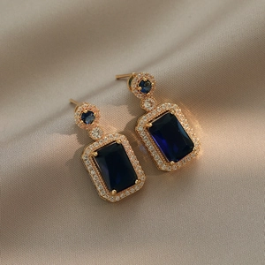 Elegant gold earrings featuring blue rectangular gemstones surrounded by small crystals