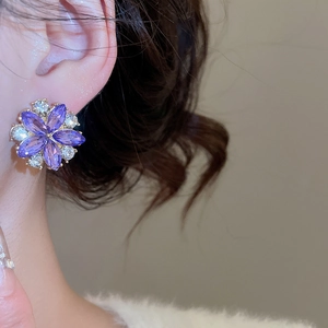 Detail view of elegant flower stud earring with purple marquise crystals on a female model