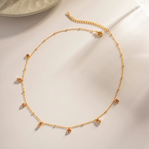 Détail du collier doré avec des pendentifs en pierres roses rectangulaires et rondes