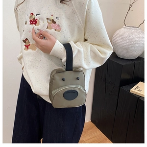 Close-up of green nylon handbag with cute cartoon eyes and nose held by a model