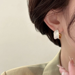 Detail of a C-shaped 18K gold plated earring with white enamel on a fashion model