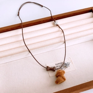 Detail of plush brown teddy bear pendant with bone charm and star tag on cord necklace