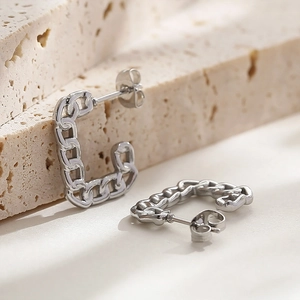 Detailed close-up of silver geometric Cuban chain link earrings on a beige stone surface