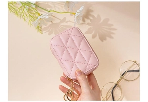 Close-up of pink quilted cosmetic bag with gold keychain held by a hand in soft light