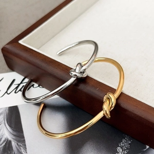 Polished gold and silver knotted metal cuff bracelets on a minimalist wooden tray