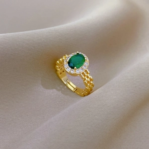 Macro detail of a gold chain-style ring featuring an oval emerald green gemstone center