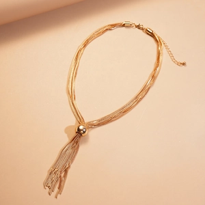 Détail du collier doré multicouche avec boule métallique et pendentif à pompon