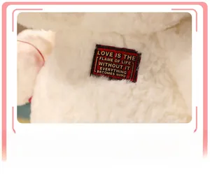 Close-up of curly white plush teddy bear showing textured fur and printed red fabric label