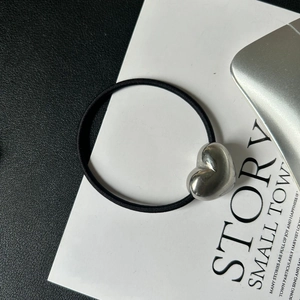 Close-up of a black elastic hair tie with a polished silver heart charm on white paper
