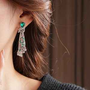 Detail of vintage heart-shaped green stone earrings with colorful dangling tassels