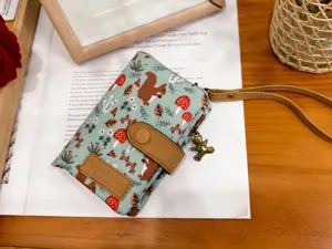 Detail of green floral fabric wallet with squirrel print, leather strap and bear charm