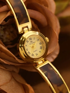 Detail of gold quartz bangle watch featuring amber tortoise shell link insets on dried flowers