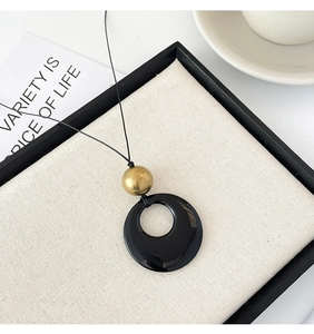 Minimalist long pendant necklace with a black round ring and gold bead on a display tray