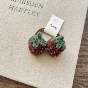 Detail of two handmade knitted strawberry hair ties with green leaves and yellow seeds