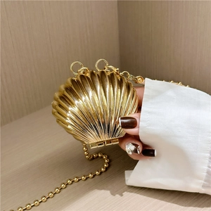 Golden shell-shaped mini metal handbag with bead chain strap held against a wooden background