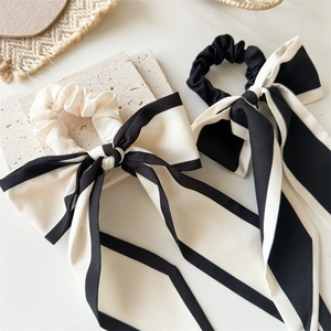 Close-up of black and white satin bow scrunchies with long ribbons on white stone