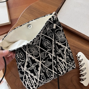 Close-up of black canvas bag with white embroidery, magnetic clasp and cord strap